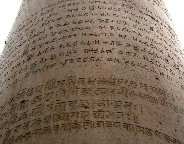 Close view of the polished stone of an Ashokan pillar, carved with rows of Brahmi script above and later Nagari script below.